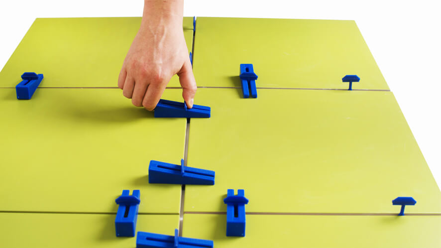 ET_pritrjevanje z roko Prikaz ročnega zategovanja Easytiler klina in spojke na rumenih ploščicah.